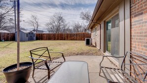 A patio with a metal table and two chairs, a wooden fence, and a building with a brick exterior. - 3 Mi to Dtwn Denton: Getaway w/ Furnished Patio! (Denton)