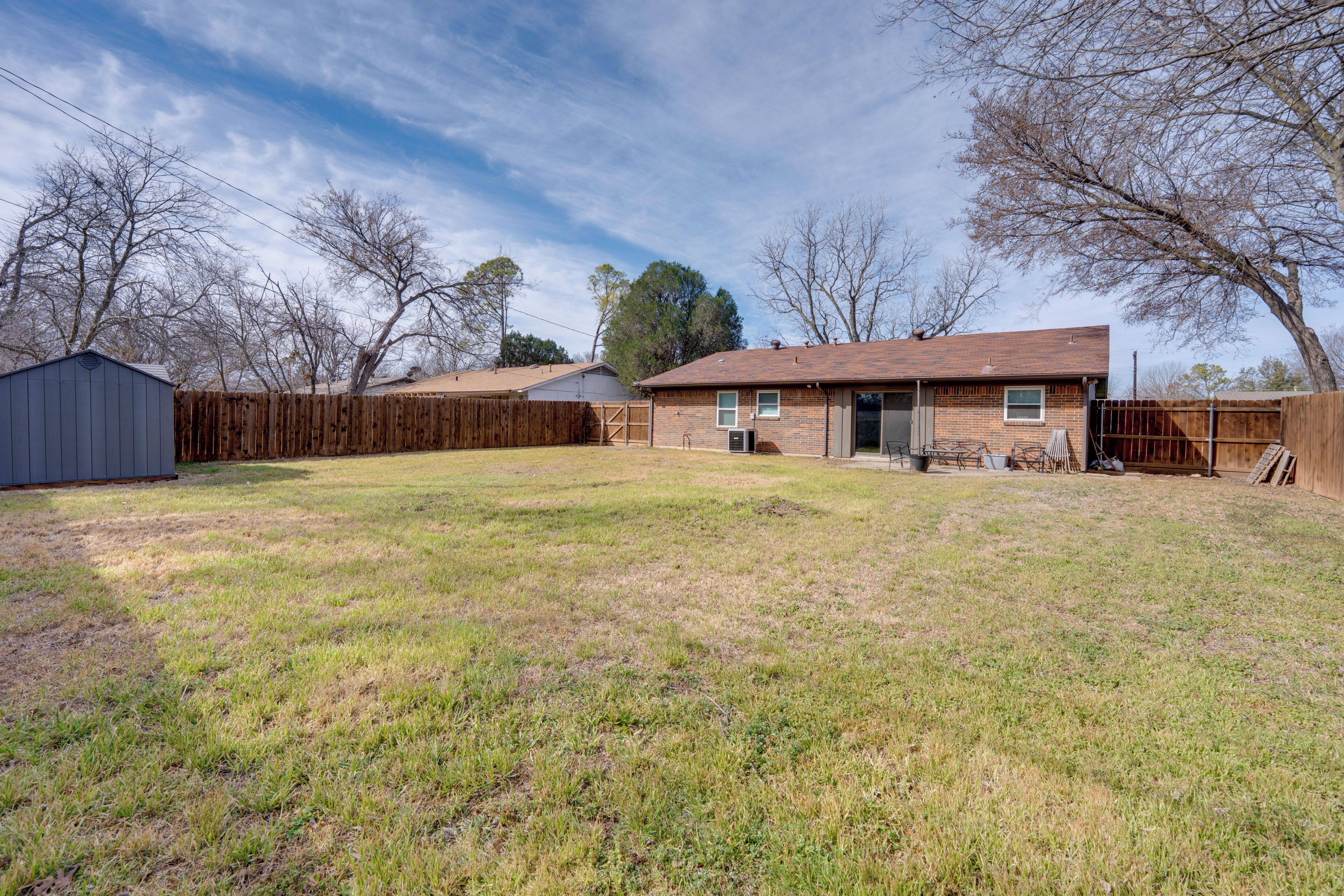 A residential backyard with a wooden fence, a shed, and a house.