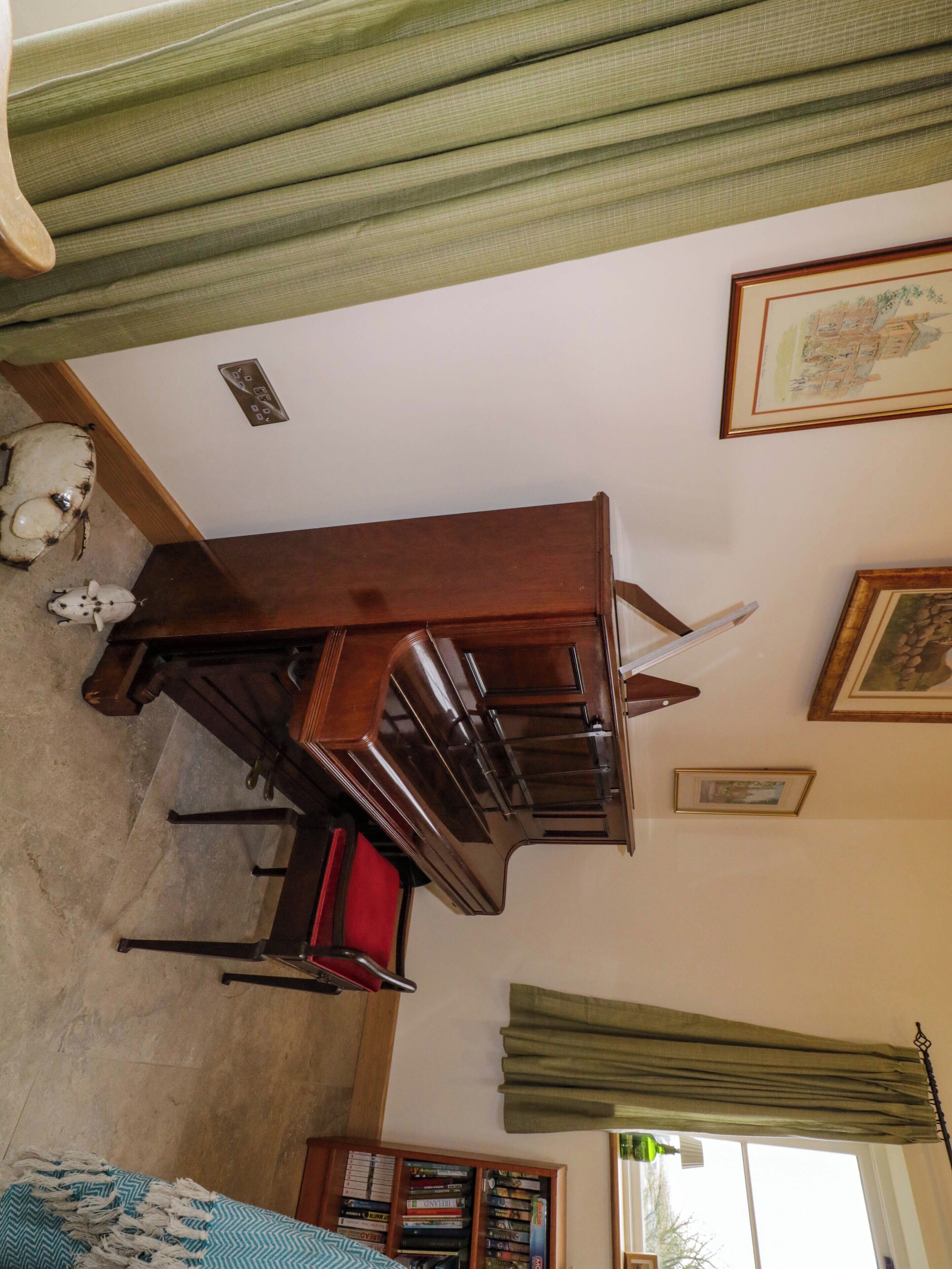 Una habitación con un piano de madera, una silla roja, una estantería y una ventana con cortinas.