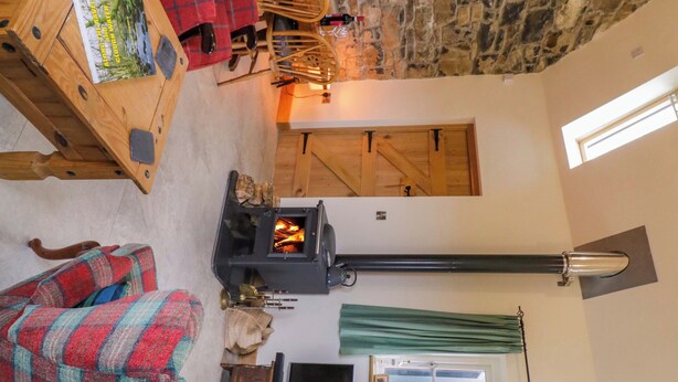 Una sala de estar acogedora con pared de piedra, una chimenea, una mesa de madera con un libro, una manta escocesa y un televisor.