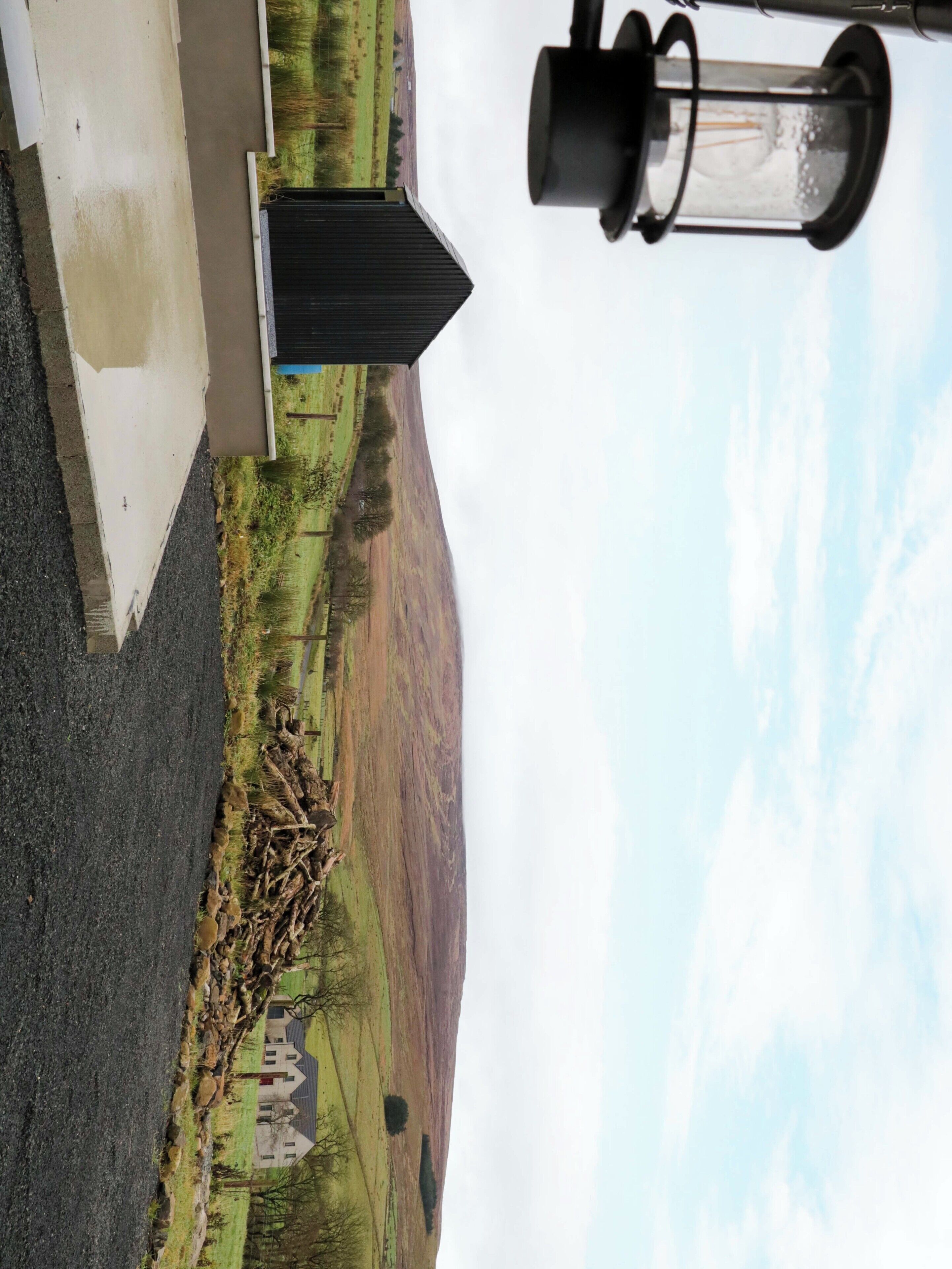 A rural landscape with a house, a pile of branches, and a lamp post.
