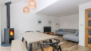 Moderni olohuone, jossa on puinen pöytä ja tuolit, sohva, televisio ja puukamiina.