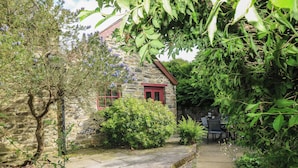 A stone building with a red door and window, surrounded by greenery and a stone pathway. - The Old Stable (Fishguard)