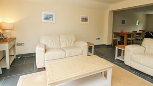 A living room with a beige sofa, a wooden coffee table, and a dining area with a wooden table and chairs. - Beachway (Newport)