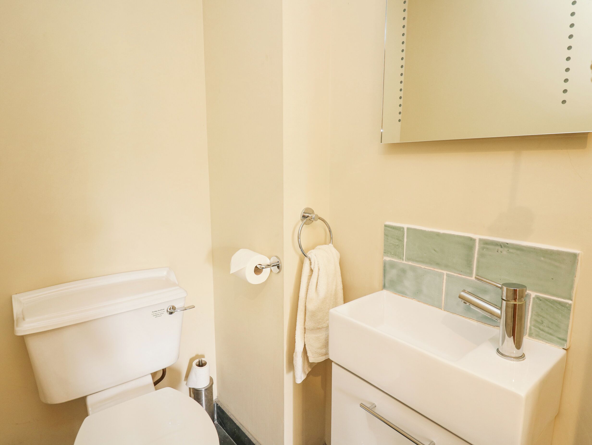 A bathroom with a toilet, sink, and mirror.