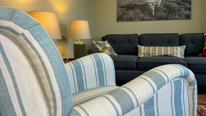 A living room with a striped armchair, a dark sofa, and a lamp. - Narrow Gauge Cottage (Ballymoney)