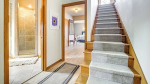A staircase leading to a bedroom with a large window, a shower area, and a framed picture on the wall.