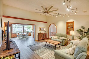 Relax in this spacious living room with a comfortable sofa and armchairs, a large window, and a door leading to an outdoor patio.