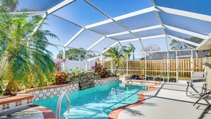 Una piscina techada con techo transparente, rodeada de palmeras y una valla de madera.