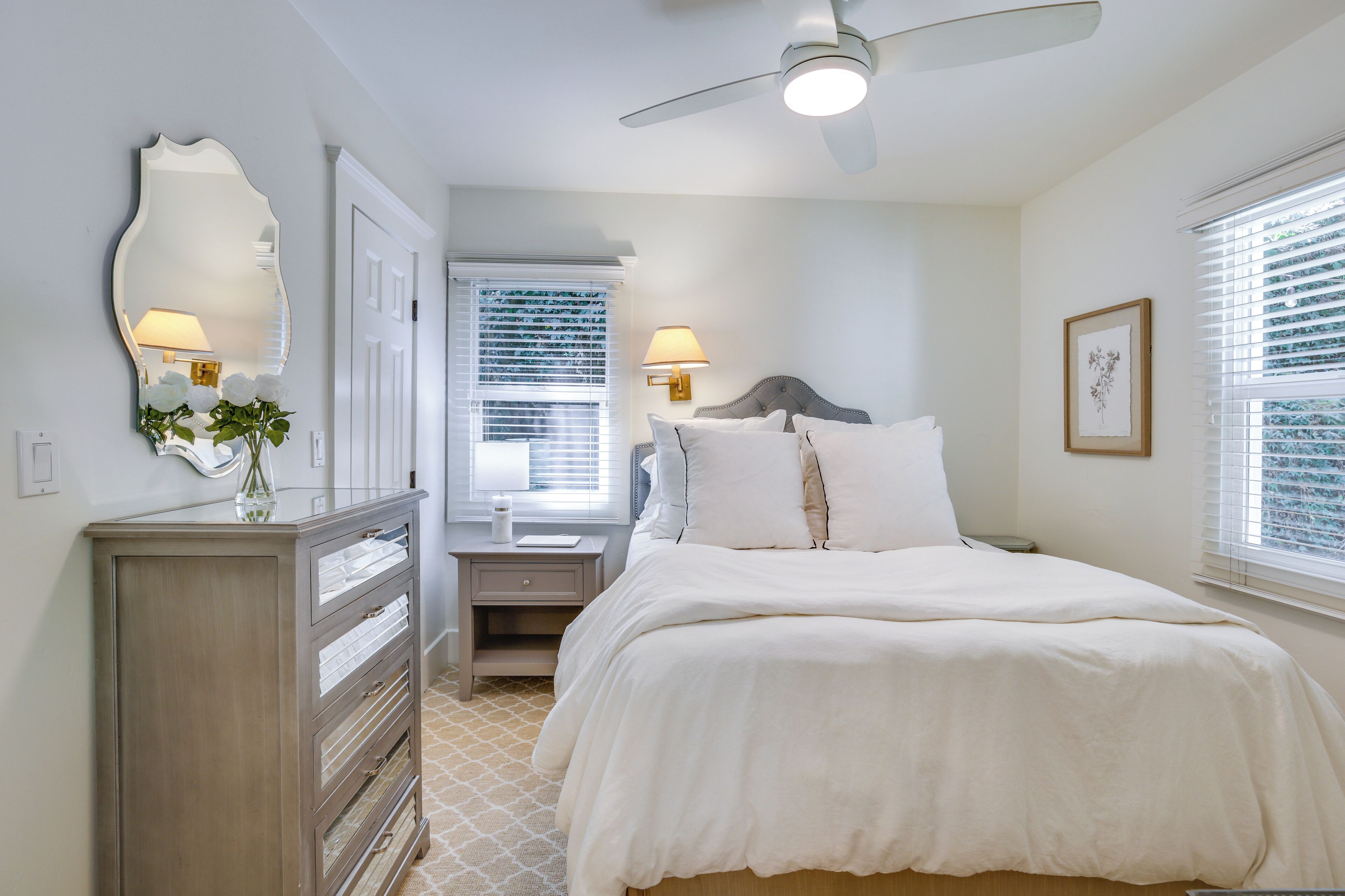 A bedroom with a bed, bedside lamps, a dresser, a mirror, and a ceiling fan.