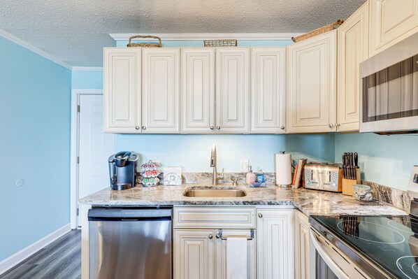 A kitchen with white cabinets, a stainless steel dishwasher, a black stove, and a marble countertop. - Scenic Oceanfront Condo in Myrtle Beach! (Myrtle Beach)