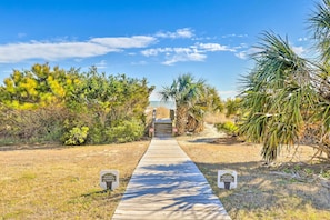 A wooden pathway leading to a private property with a clear sky and tropical vegetation.