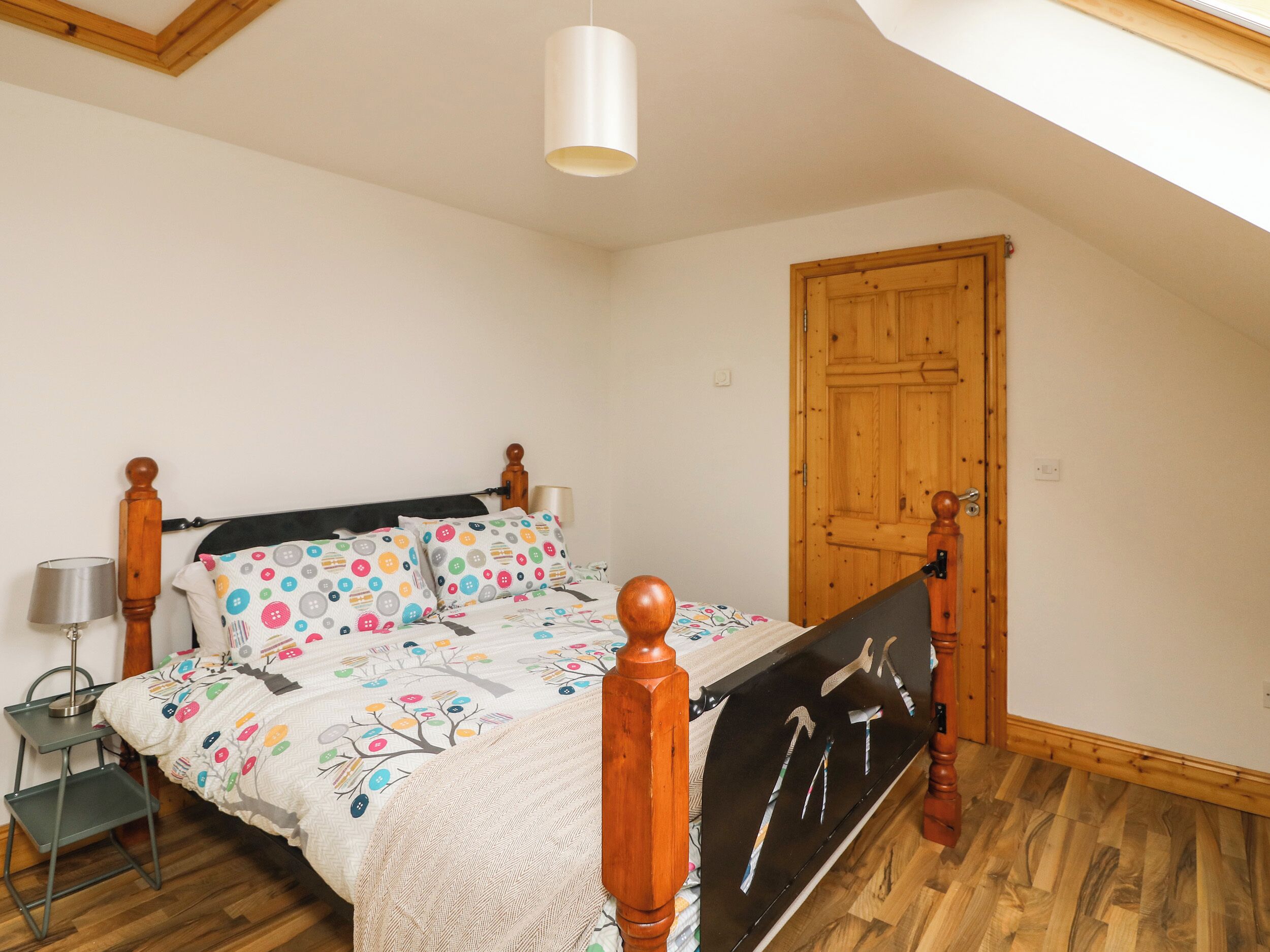 Une chambre avec un cadre de lit en bois, un ventilateur de plafond blanc, une porte en bois et un puits de lumière.