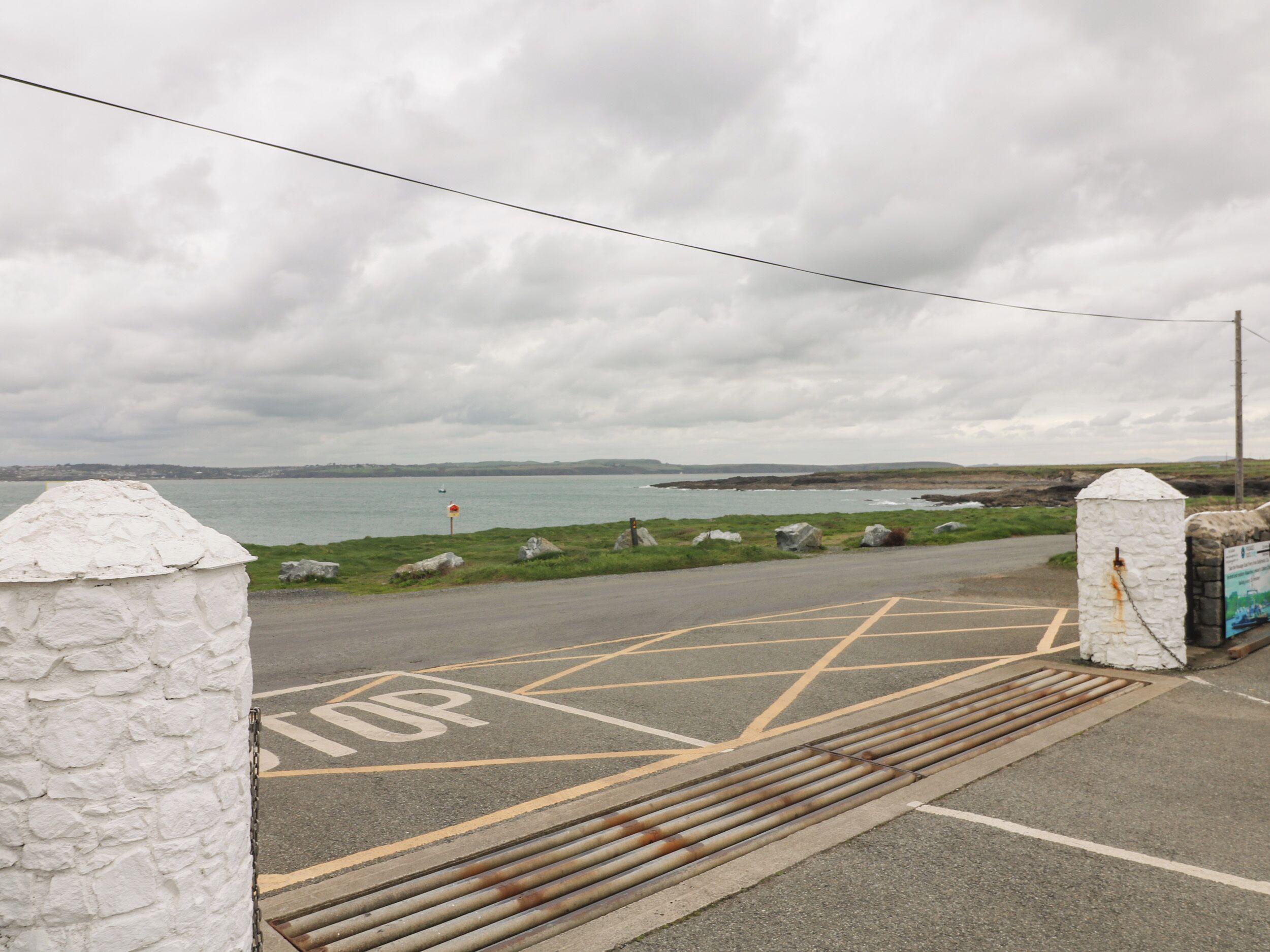A coastal road with a white stone wall, a 'No Entry' sign, and a view of the sea and distant hills.