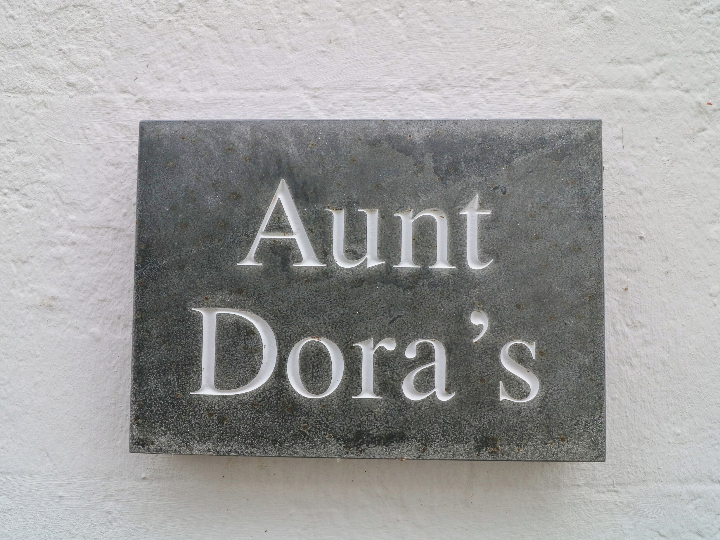 Une plaque en pierre portant l’inscription « Chez Tante Dora » est fixée à un mur.