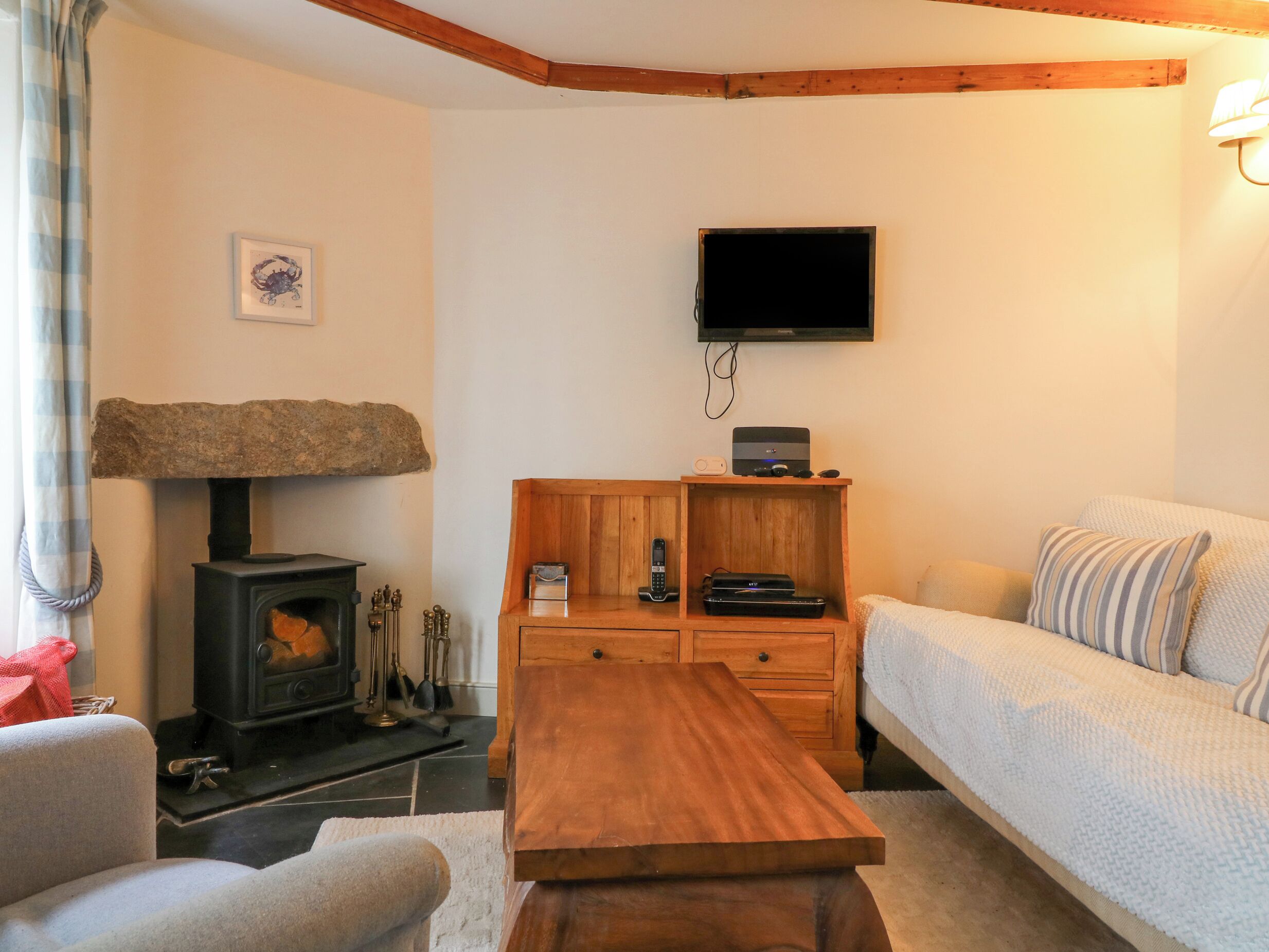 A cozy living room with a stone fireplace, a wooden coffee table, a sofa, and a television mounted on the wall.
