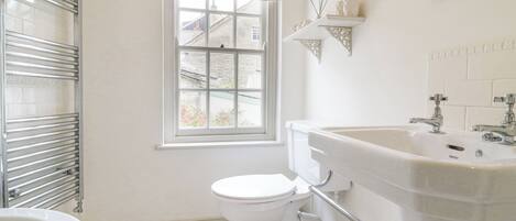 A bathroom with a white toilet, a white sink, and a bathtub. There is a window with a floral curtain and a view of buildings outside.
