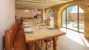 A dining area with a wooden table set for six, surrounded by stone walls and large windows.