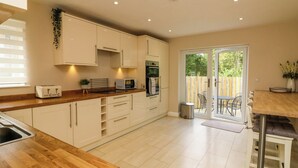 A modern kitchen with wooden countertops, white cabinets, and a sliding glass door leading to an outdoor patio. - Spicery (Exeter)