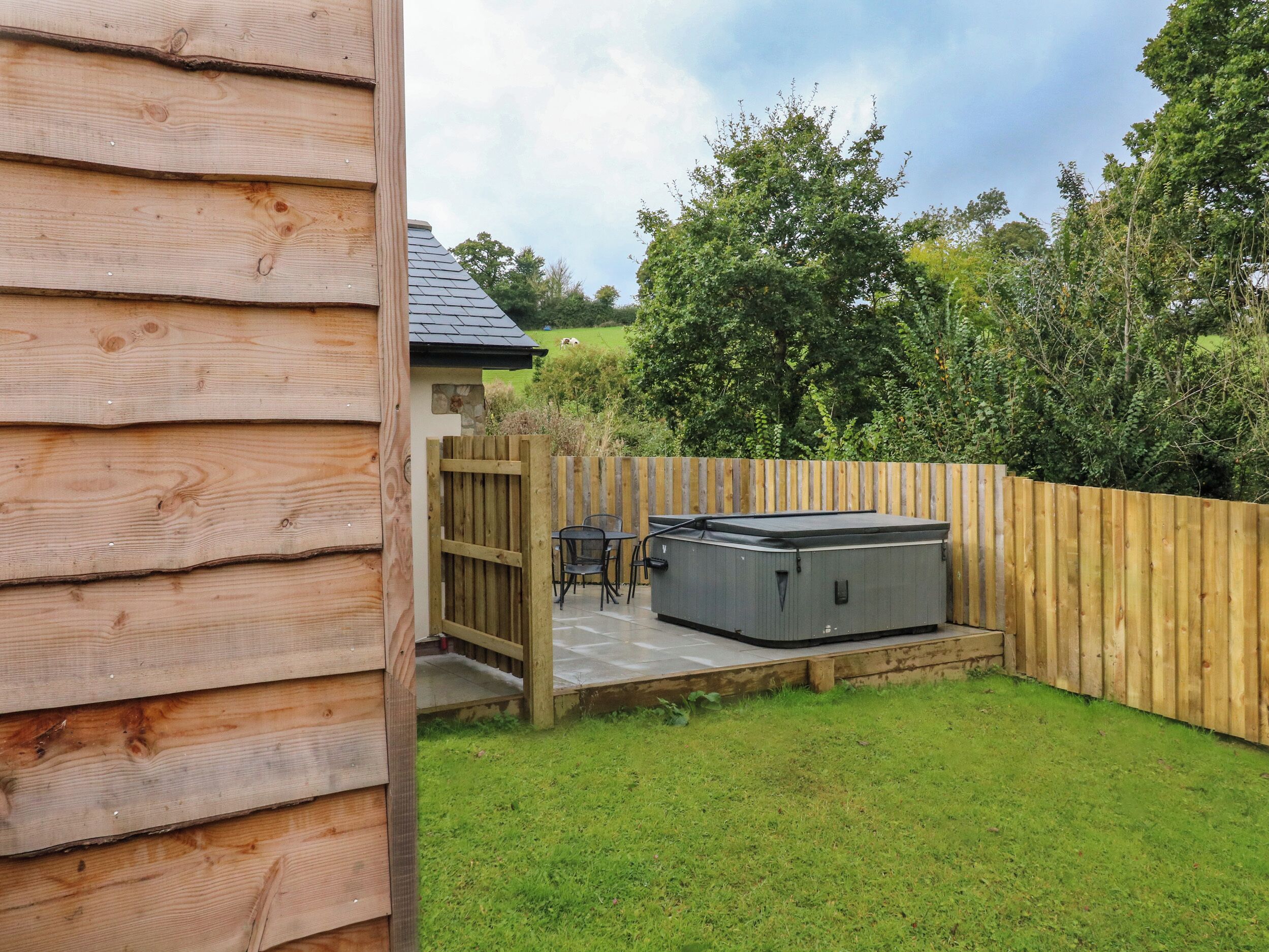 A wooden cabin with a hot tub in the backyard, surrounded by a wooden fence and lush greenery.