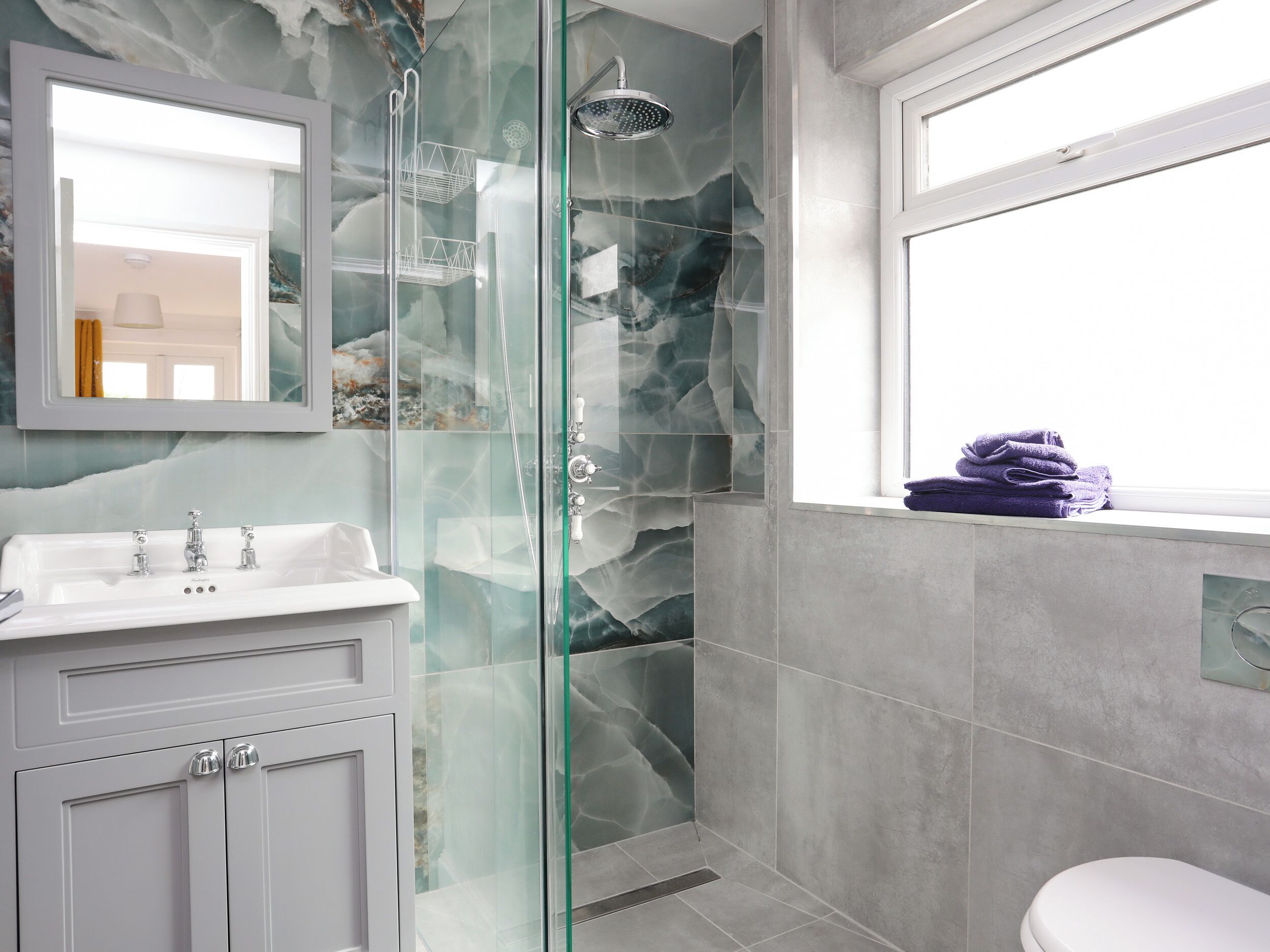A bathroom with a glass-enclosed shower, a white sink, and a window.