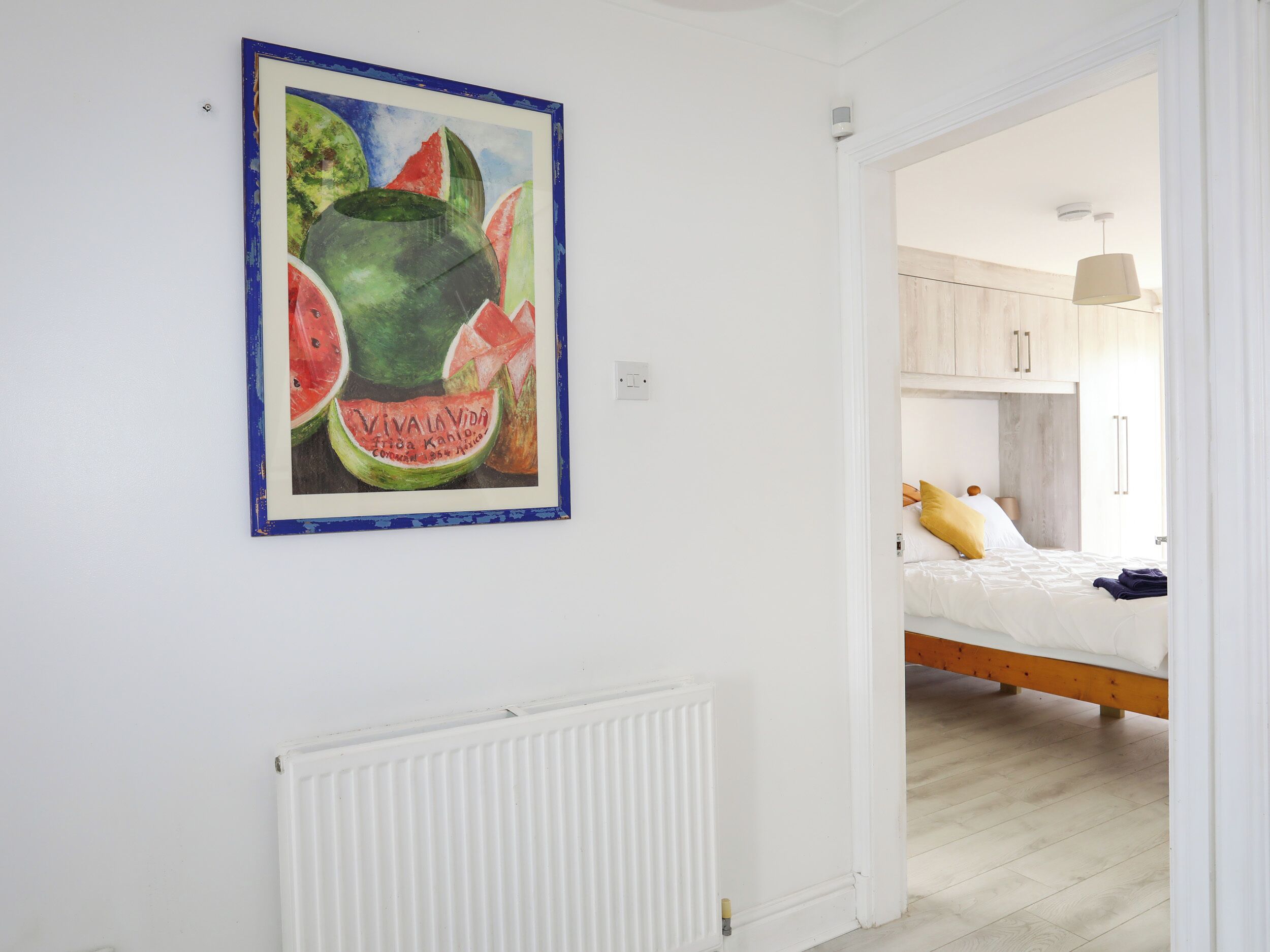 A bedroom with a bed, a nightstand, and a wall-mounted painting of fruit.