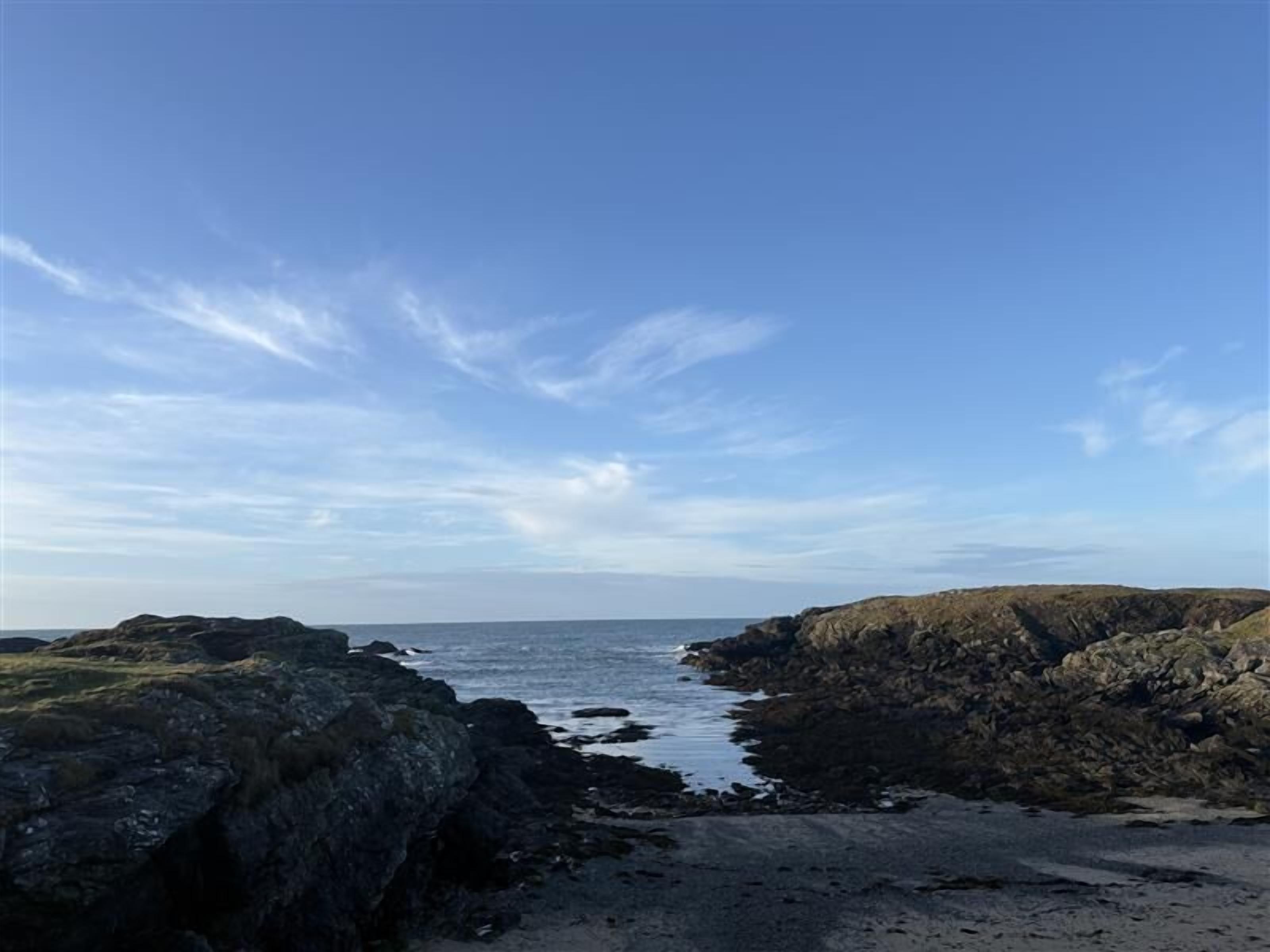 A coastal landscape with rocky terrain and a clear sky.