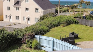 A two-story building with a flat roof and multiple windows, surrounded by a well-maintained garden and a view of the sea. - Seaside Sanctuary (Holyhead)