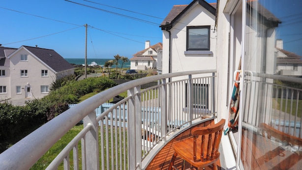 A balcony with a wooden chair, overlooking a coastal residential area with houses and the sea. - Seaside Sanctuary (Holyhead)