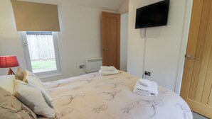 A bedroom with a bed, a TV, a window with blinds, a radiator, and a door. - Mallard Lodge (Galston)
