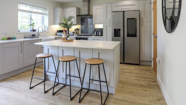 A modern kitchen with a central island, bar stools, stainless steel appliances, and a large window.