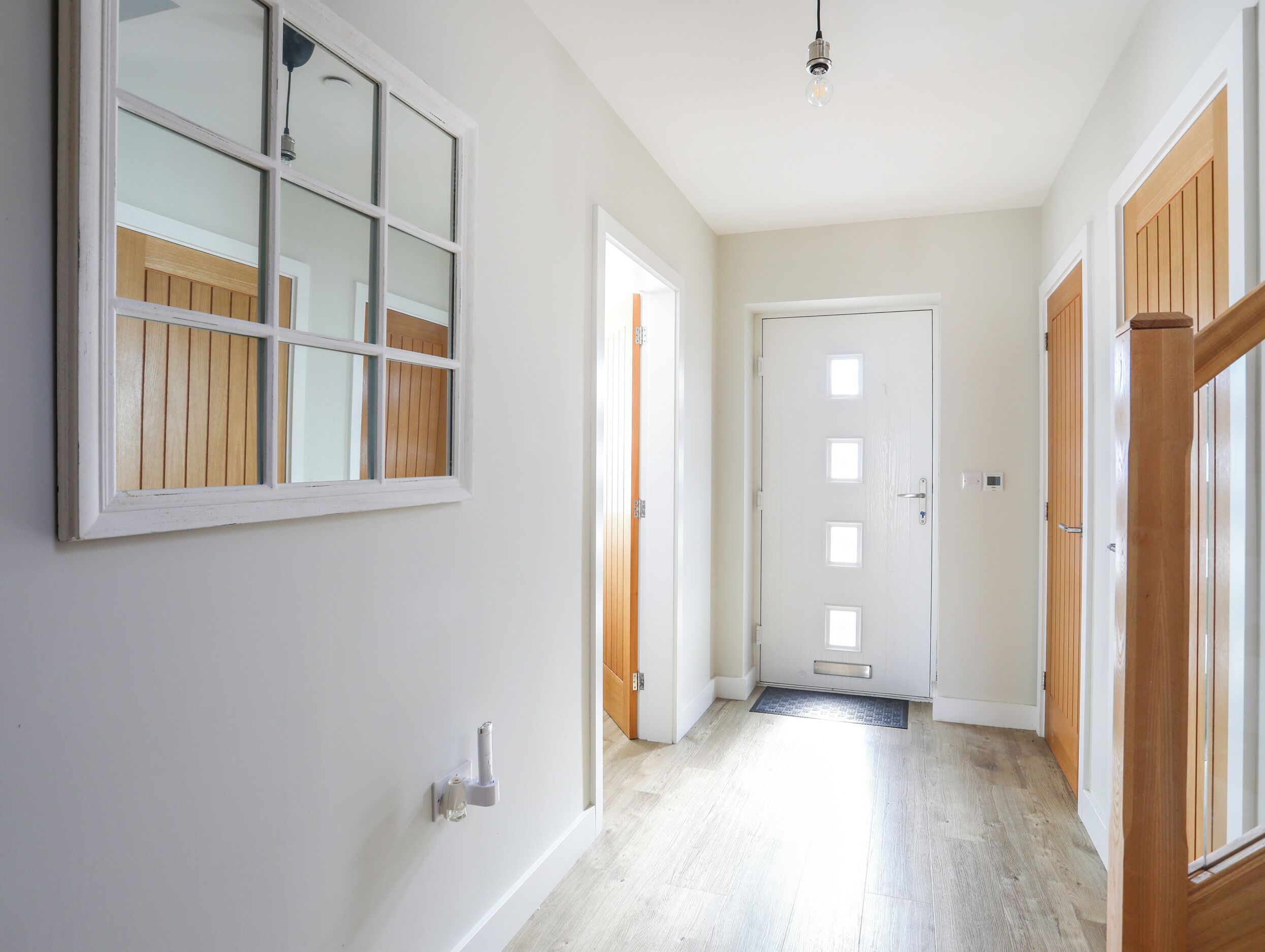 A hallway with white walls, wooden doors, and a light wooden floor.
