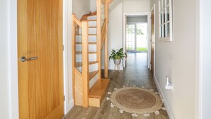 A wooden staircase with a glass railing leading to a door. A woven rug is on the floor, and a potted plant is visible.