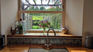 Una cocina con vista al jardín, un lavamanos, una tetera y un microondas.