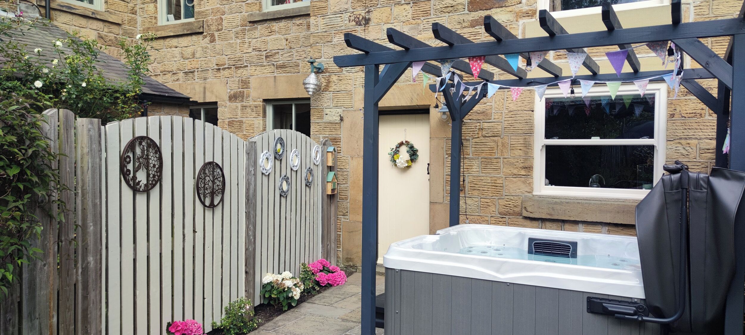 Une porte en bois ornée de plaques de métal décoratives, un jacuzzi et une pergola décorée de guirlandes.