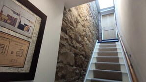 Una escalera lleva a una puerta de madera, con una pared de piedra y planos arquitectónicos enmarcados en la pared.