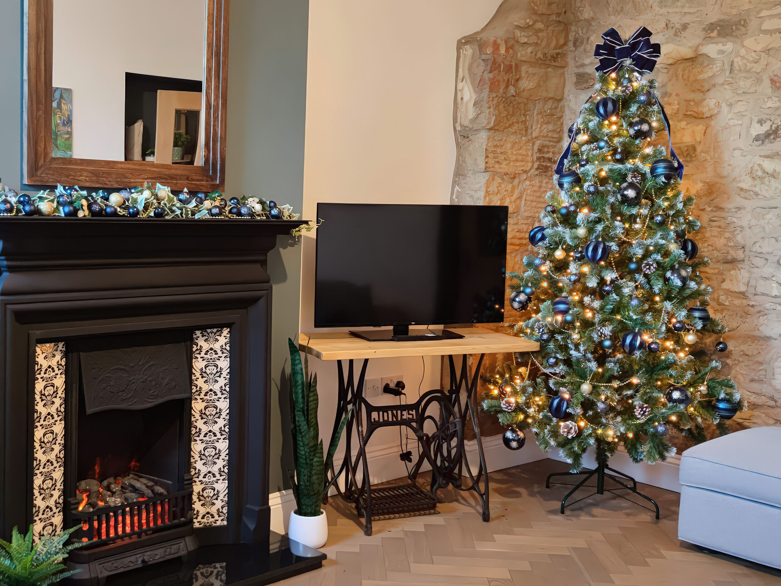 A living room with a fireplace, a television on a wooden stand, a Christmas tree, and a stone wall.