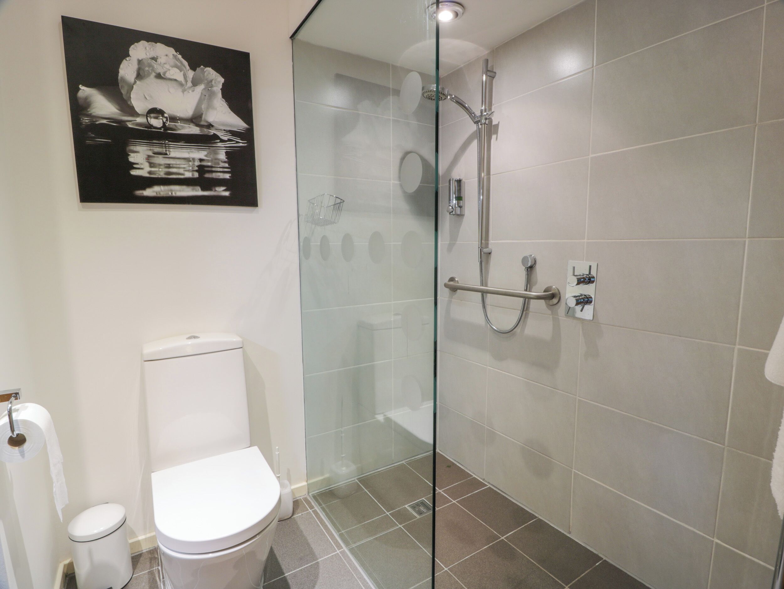 A modern bathroom with a glass-enclosed shower, a toilet, and a towel rack.