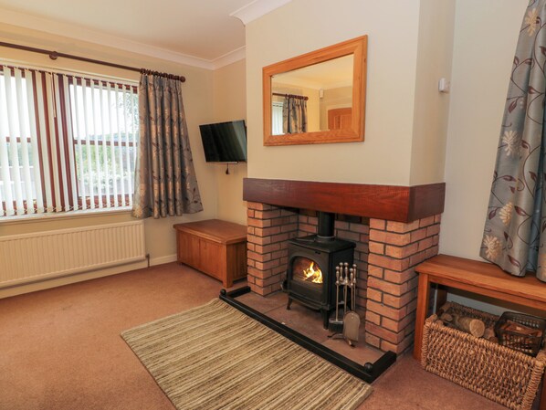 A cozy living room with a brick fireplace, a television mounted on the wall, and a window with curtains. - The Barn at Daldorch (Mauchline)