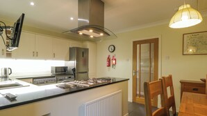 A modern kitchen with a central island, built-in appliances, and a dining area with wooden furniture. - The Barn at Daldorch (Mauchline)