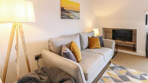 Un salon avec un canapé, une lampe, un téléviseur et un tableau accroché au mur.