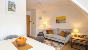 Un salon moderne avec un canapé, une table sur laquelle se trouve un saladier rempli de fruits, une lampe et une radio posée sur une table d’appoint.
