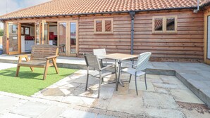 Eine Holzhütte mit Ziegeldach, einer Terrasse mit Steinböden und einer kleinen Sitzgelegenheit im Freien mit Tisch und Stühlen.