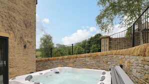 A hot tub with stone walls and a metal fence, surrounded by greenery. - Ty Gambo (Matlock)