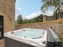 Un jacuzzi con paredes de piedra y valla metálica, rodeado de follaje.