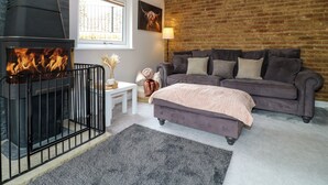 Une pièce chaleureuse avec une cheminée, un mur en briques, un canapé gris et une fenêtre.