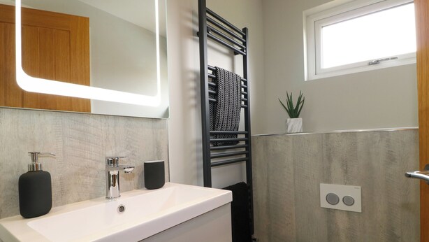 A modern bathroom with a white sink, black towel, and a small potted plant. - Ty Gambo (Matlock)