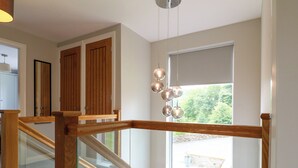 Un intérieur moderne avec un escalier en bois, une grande fenêtre donnant sur un espace verdoyant et un luminaire suspendu.