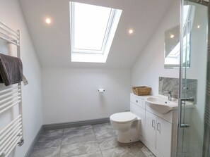 Une salle de bain moderne dotée d’une lucarne, de toilettes blanches, d’un lavabo avec un pare-éclaboussures en marbre et d’une douche à parois de verre.