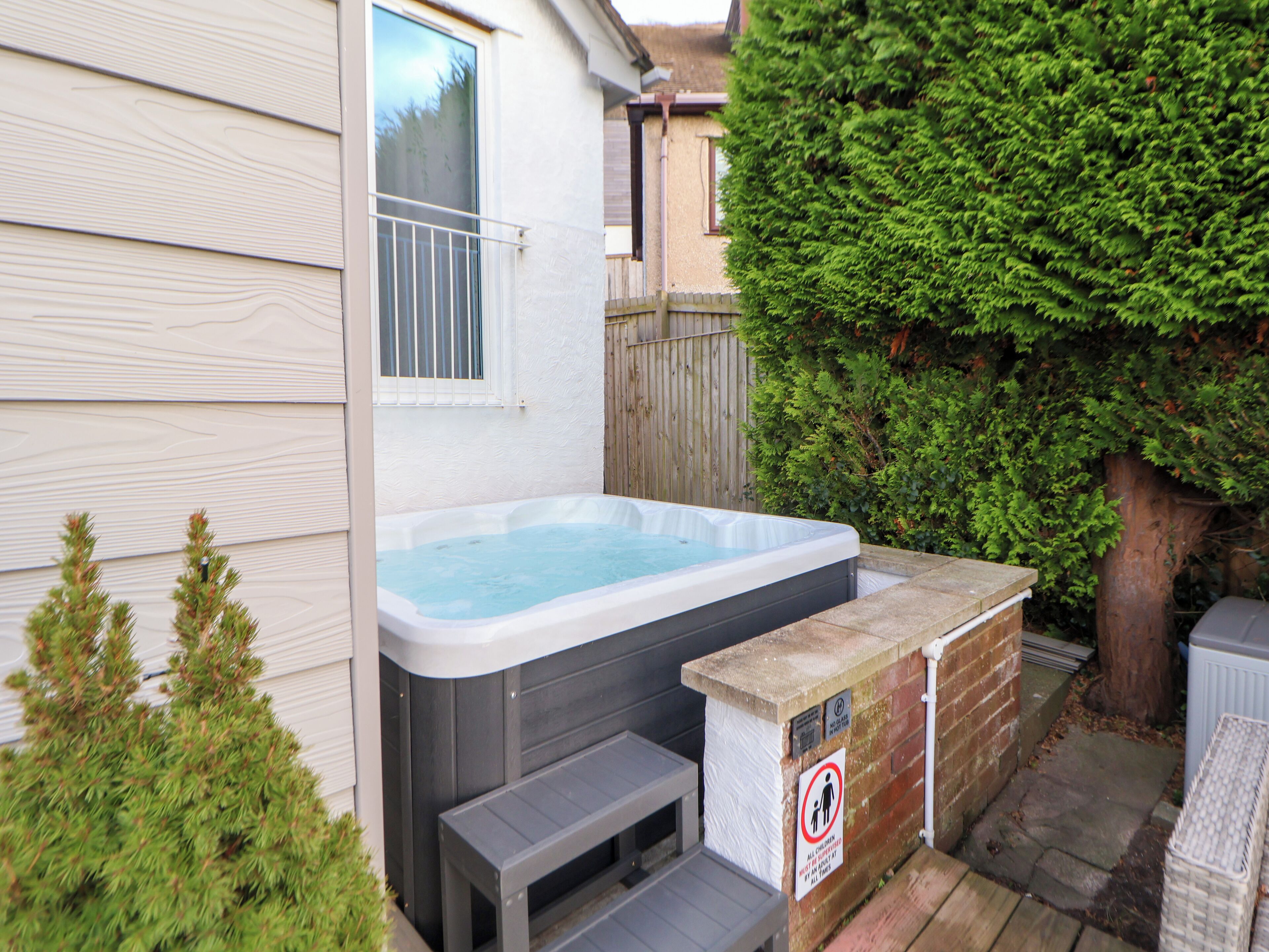 A hot tub in a backyard with a wooden deck and a brick wall.